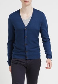 Marinblå cardigan med V-hals, knäppning fram och ribbade ärmslut och nederkant. Tillverkad av ett mjukt, stickat tyg med en slät yta.