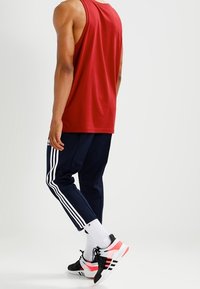 Červený bezrukávový top, námořnické tepláky s bílými pruhy, černé a růžové sportovní boty a bílé ponožky. Hladká textura látky.