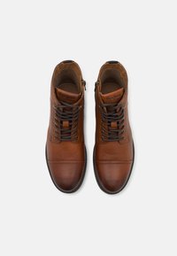 Brūni ādas augstpapēžu apavi ar auklu un rāvējslēdzēja aizdari, ar gludu apdari un minimālām šuvju detaļām.