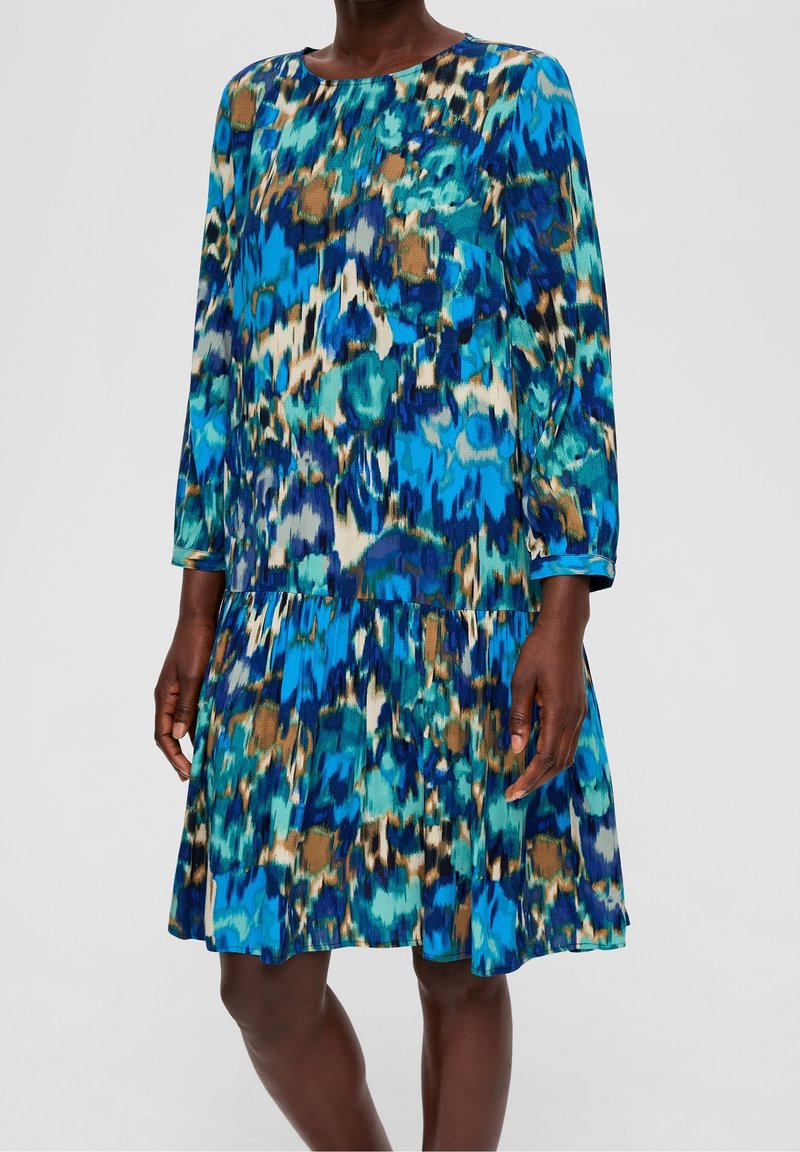 Blau- und grün gemustertes Kleid mit langen Ärmeln, rundem Ausschnitt und gestuftem Rock. Leichter Stoff mit fließender Textur und sanftem Fall.