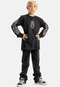 Zwarte langetermijnshirt met vlamgraphics op de mouwen, zwarte broek en meerkleurige sneakers met grijze en oranje accenten.