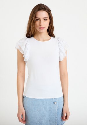 Jonge vrouw met golvend bruin haar, gekleed in een witte top met geplooide korte mouwen en een lichtblauwe rok met kleine witte bloemenborduurwerk.