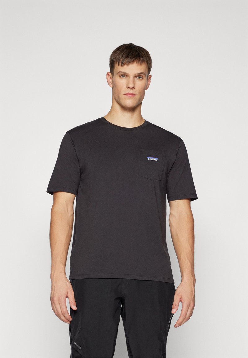 Tricou din bumbac negru cu decolteu rotund, mâneci scurte și un buzunar pe piept cu un mic logo albastru. Materialul are o textură netedă.