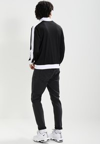 Black jacket with white side stripes, ribbed hem and cuffs. Paired with black jeans and white athletic shoes. Smooth fabric, casual fit.