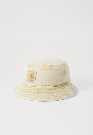 Vaalean beige bucket-hattu, joka on valmistettu puuvillasta ja siinä on teksturoitu kuvio. Edessä on oranssi-valkoinen logo-painatus. Litteä, leveä lippa.