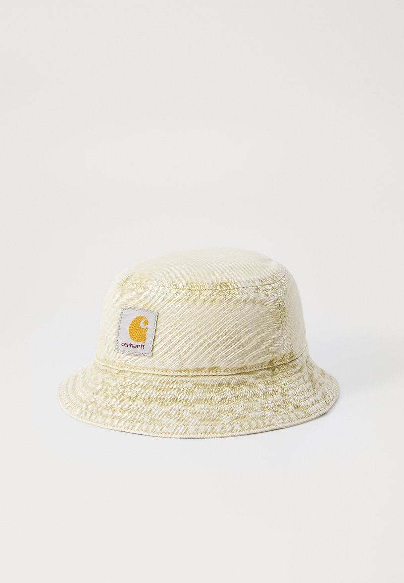 Lys beige bucket hat lavet af bomuld med et tekstureret mønster. Har et logo-patch i orange og hvid på forsiden. Flad, bred skygge.