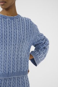 Suéter de punto trenzado en azul claro con cuello redondo acanalado. Presenta patrones verticales texturizados y mangas con puños. Material suave y acogedor.