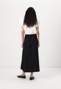 Haut blanc à manches courtes et volants associé à une longue jupe noire fluide ; modèle vu de dos, portant des ballerines noires.