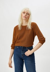Brązowy sweter z prążkowanego dzianiny z długimi rękawami, w połączeniu z niebieskimi jeansami o wysokim stanie. Materiał ma teksturowany wygląd i luźny krój.