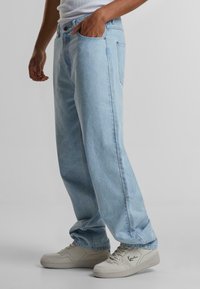 Jeans din denim de culoare albastru deschis, cu o croială lejeră, având cinci buzunare și cusături contrastante, asortați cu adidași albi.
