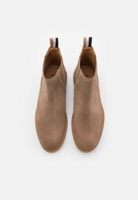 Brązowe zamszowe botki Chelsea z elastycznymi bocznymi panelami, zaokrąglonymi noskami i teksturowaną podeszwą. Posiada paski do chwytania z tyłu.