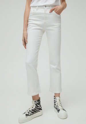 Person wearing high-waisted white jeans cropped above the ankle paired with black-and-white zebra-patterned high-top sneakers.