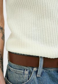 Gebreide crèmekleurige tanktop met een geribbelde textuur, gecombineerd met blauwe denim jeans met een bruine leren riem en zichtbare hardware op de zakken.