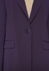 Fioletowa marynarka z jednym guzikiem, klapami z wycięciami oraz dwoma przednimi kieszeniami, wykonana z gładkiej, drobno teksturowanej tkaniny.