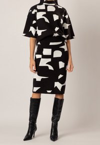 Pletený svetr s krátkými rukávy, zdobený výrazným černo-bílým abstraktním vzorem. Přiléhavá černá tužková sukně a černé kozačky po kolena.