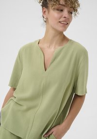 Lichtgroene tuniek met een V-hals, korte mouwen en een ontspannen pasvorm. Heeft een zachte, gestructureerde stof en zijzakken.