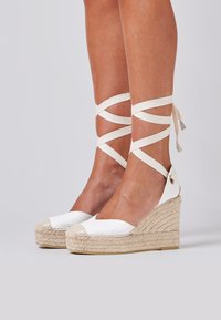 Sandalias de cuña espadrille blancas con suela de yute texturizada, que cuentan con tiras de tela cruzadas alrededor del tobillo y un diseño de puntera redondeada.