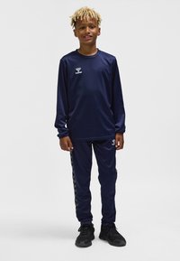 Marinblå sportset med långärmad tröja och byxor, tillverkat av mjukt tyg med en logotyp på bröstet och logotryckta sidodetaljer.