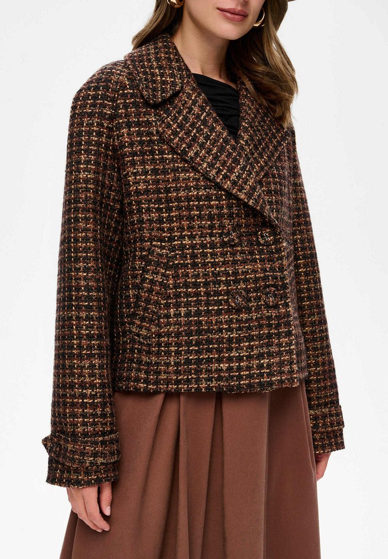 Brauner karierter Blazer mit einer doppelt knöpfbaren Vorderseite, breiten Revers und strukturiertem Stoff. Lange Ärmel mit Manschetten-Details.