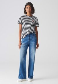 Gestreepte zwart-witte t-shirt met een rode accent, gecombineerd met blauwe wijdte jeans en witte sneakers. Glad stof, casual pasvorm.