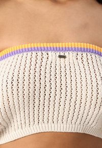 Top sans bretelles en tricot crème, présentant un col côtelé multicolore avec des accents orange, violet et bleu clair. Petit détail en métal avec logo.