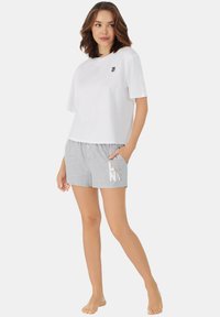 Weißes T-Shirt mit kurzen Ärmeln und DKNY-Logo auf der Brust, kombiniert mit grauen Shorts, die ein diagonales weißes und pinkes Grafikmuster aufweisen.