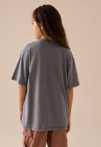 T-shirt gris surdimensionné en coton avec une silhouette décontractée et des manches courtes, présentant un col rond et des coutures apparentes.