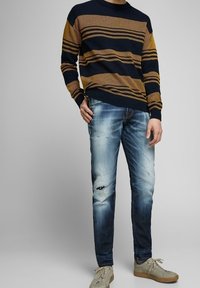 Marinblå och senapsgul randig stickad tröja i kombination med ljusblå slitna jeans. Skorna är beige med en strukturerad yta.