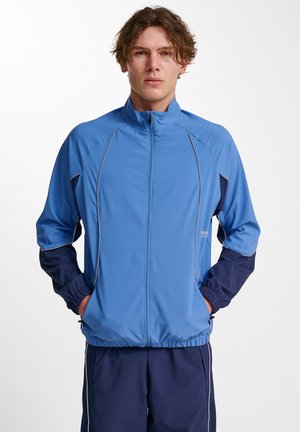 Lichte blauwe zip-up jas met marineblauwe mouwen, elastische manchetten en zoom, met een gladde textuur en subtiele reflecterende details.