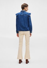 Τζάκετ από τζιν με φαρδιά ώμους, μπλε χρώμα και μεταλλικές λεπτομέρειες. Συνδυάζεται με κρεμ φαρδιά παντελόνια και καφέ μποτάκια με τακούνι.