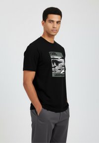 Musta puuvillainen t-paita, jossa on edessä kontrastivärinen "Karl Lagerfeld" -grafiikka. Lyhyet hihat ja pyöreä pääntie.