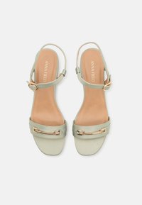 Paire de sandales ouvertes vert clair pour femmes avec brides à la cheville, boucle dorée et barre décorative sur les brides avant.