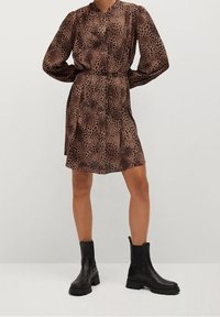 Ruskean leopardi-tyylinen mekko, jossa on pitkät hihat, nappikiinnitys ja vyöyksityiskohta. Yhdistetty mustiin, paksupohjaisiin nilkkabootseihin, joissa on teksturoidut pohjat.