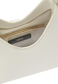 Crème leren handtas met een gestructureerd oppervlak, voorzien van een binnenzak met rits en een zwart label met "FURLA" in goud geperst.