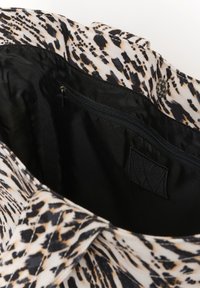Leopard print fabric bag with a black interior, featuring a zippered pocket and a snap closure detail. Textured surface with bold patterns.