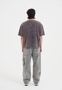Gray oversized t-shirt with a dragon graphic on the back paired with light gray cargo jeans featuring contrasting white embroidery and pockets.