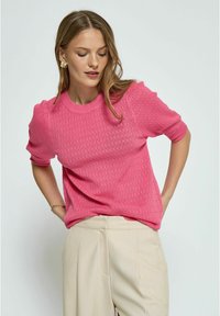 Rosa gestrickter Pullover mit kurzen Ärmeln, strukturiertem Muster, Rundhalsausschnitt und lässiger Passform, kombiniert mit hellbeigen Hosen.