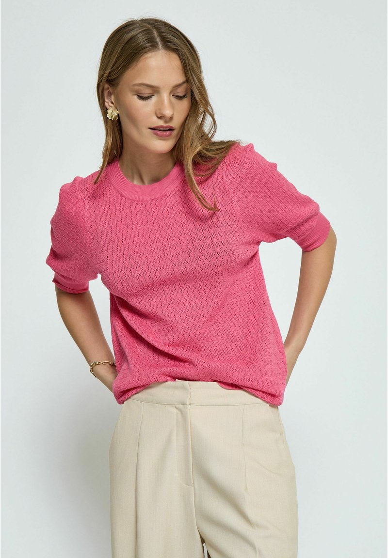Roze gebreide trui met korte mouwen, voorzien van een textuurstiksel, ronde halslijn en een comfortabele pasvorm, gecombineerd met lichtbeige broeken.