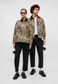 Leopárdmintás kabátok fekete gallérral, fekete nadrágokkal párosítva, amelyeken derékra kötőszalag található. A modellek fekete mokaszinokat és napszemüveget viselnek.