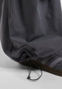 Šedé zúžené kalhoty s elastickými manžetami, detaily na leme, spárované s tmavě šedou obuví se třemi texturovanými pruhy.