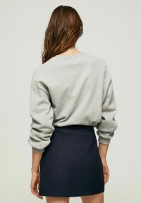 Šedá mikina s dlouhými rukávy, kulatým výstřihem a volným střihem; zkombinovaná s tmavě modrou mini sukni se švovými detaily a hladkou texturou.