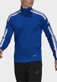 Haut de sport bleu à manches longues avec un col zippé mi-hauteur, rayures blanches sur les épaules et logo "AEROREADY" en bas. Tissu lisse et ajusté.