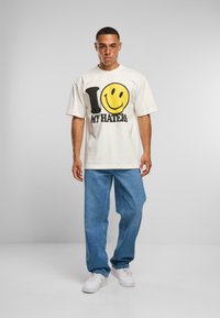 Hvit bomulls t-skjorte med et stort svart og gult grafisk design som står "I ♥ MY HATERS." Brukt med avslappede blå denim jeans og hvite joggesko.
