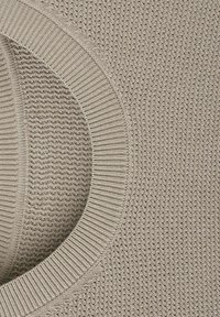 Tissu tricoté beige avec un col côtelé et un motif texturé couvrant la surface.
