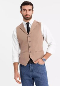 Beige, strukturiertes Weste mit Revers, fünf Knöpfen und zwei vorderen Taschen, kombiniert mit einem weißen Hemd und einer dunklen Krawatte.
