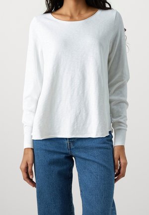 Long-sleeve white top made of lightweight fabric, with a rounded neckline and a relaxed fit. Paired with blue jeans.