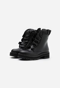 Botas negras de cuero hasta el tobillo con parte superior de textil con volantes, acentos texturizados y suela de goma gruesa con costuras decorativas.