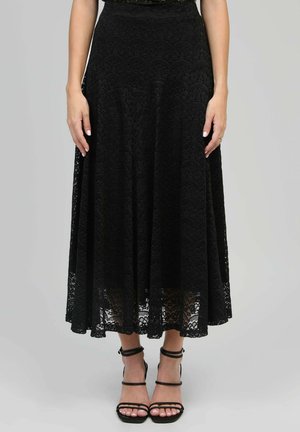 Jupe en dentelle noire avec un design évasé, présentant un motif texturé. Assortie à des sandales noires à lanières. Élégante et longue jusqu'au sol.