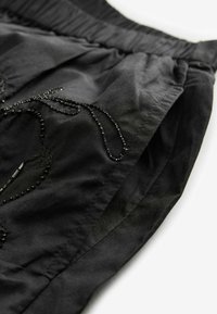 Schwarzes Stoffkleid mit strukturierter Oberfläche, verziert mit filigraner Perlenarbeit und einem gerafften elastischen Bund für eine verstellbare Passform.