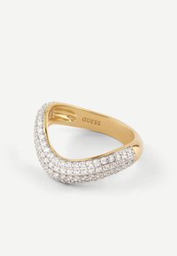 Złoty pierścionek o zakrzywionym wzorze, z rzędem małych, przezroczystych, błyszczących kamieni osadzonych na górze. Wyryte "GUESS" wewnątrz obrączki.